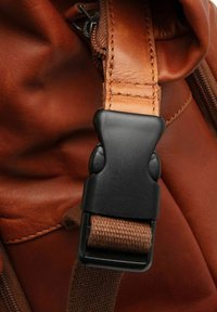 Bolso de cuero marrón con un cinturón de plástico negro y una correa texturizada marrón; las costuras visibles y los detalles de la cremallera mejoran su funcionalidad.
