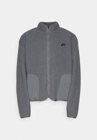 Giacca in pile grigia con colletto alto, zip frontale e tessuto strutturato. Presenta dettagli grigi sui taschini e un piccolo logo nero sul petto.