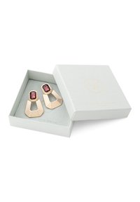 Pendientes geométricos en tono dorado con piedras rectangulares rojo oscuro en una caja de joyería blanca con la marca Nordic Design Jewellery.