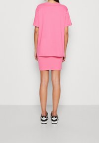 Rosa bomullsoverdel i oversize-storlek, kombinerad med en ribbad rosa minikjol, bärs med svartvita sneakers med en logotyp på hälen.