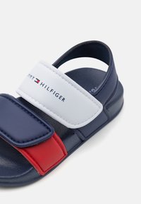 Granatowe i czerwone sandały z dwoma regulowanymi paskami, z białą wstawką z wytłoczonym logo "TOMMY HILFIGER". Teksturowana podeszwa dla lepszej przyczepności.