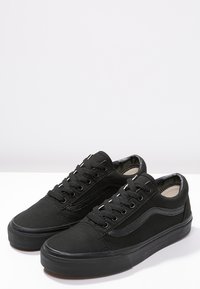 Sneaker in tela nera con profilo basso, design con lacci, suola in gomma e dettagli testurizzati sui lati. Stile minimalista.