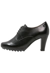 Chaussure noire en cuir à talon avec un bout pointu, des coutures décoratives et une semelle en caoutchouc dotée d'un motif de profilé. Design de tige légèrement allongé.