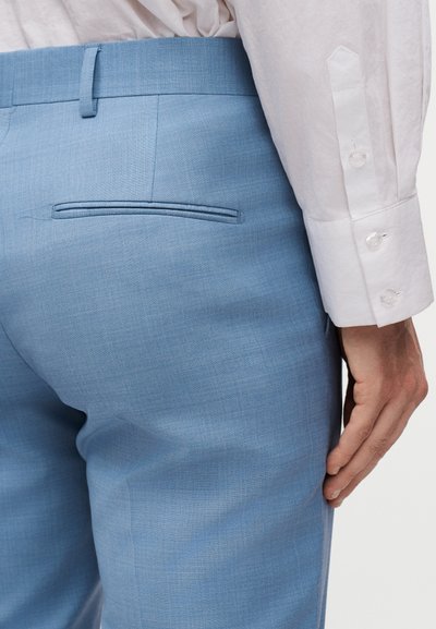 Κοντινό πλάνο ατόμου που φοράει ανοιχτό μπλε παντελόνι με πίσω τσέπη και λευκό πουκάμισο με μακριά μανίκια και κουμπωτό μανσέτα.