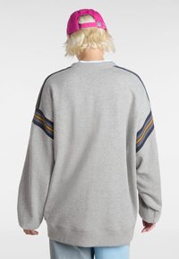 Grijze sweatshirt met lange mouwen, geribde zoom en zijsrepen in marineblauw en geel. Gemaakt in combinatie met een roze pet. Zachte stoffen textuur.