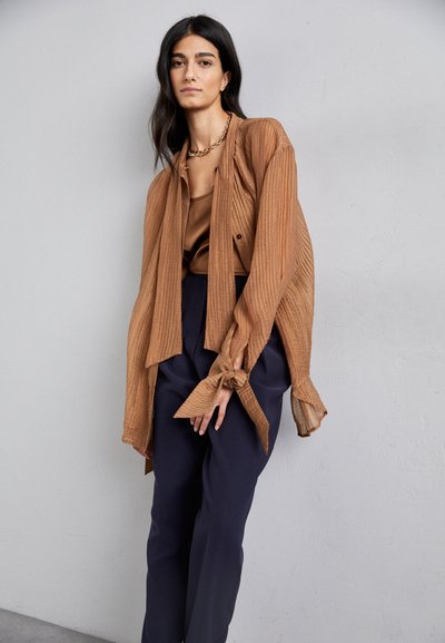 Brown ribbed layered shirt with tie sleeves worn over a brown satin top and navy wide-leg trousers. Simple design, textured fabric.