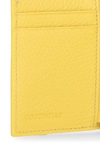 Żółty skórzany holder na karty o teksturowanej powierzchni, z czterema miejscami na karty i wytłoczonym logo "Coccinelle" na dole. Czysty, minimalistyczny design.