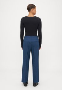 Zwart longsleeve bodysuit gecombineerd met high-waisted, wijde donkerblauwe broek van een textuurstof en met achterzakken.