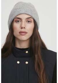 Cappello di lana grigio a maglia con texture a coste, indossato con un gilet trapuntato blu navy con dettagli in hardware dorato e colletto alto.