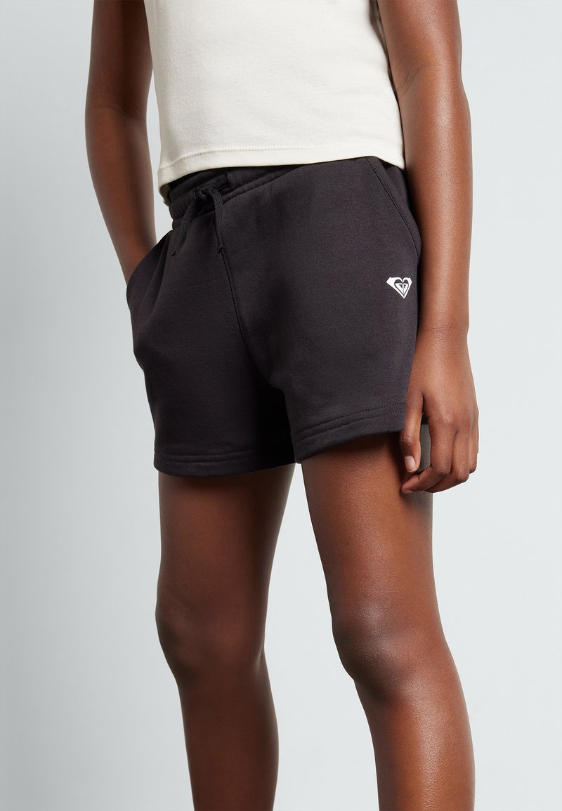 Shorts en coton noir avec taille élastique à cordon de serrage, dotés de poches latérales, et d'un petit logo blanc sur le devant. Texture lisse.