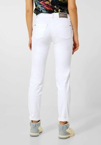 Witte denim jeans met een slim fit en opgerolde manchetten, met een middelhoge taille en twee achterzakken. Gdraagd met lichtgekleurde sneakers.