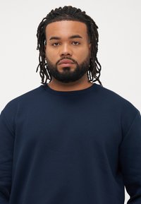Marineblaues Rundhals-Sweatshirt mit langen Ärmeln, aus glattem Stoff gefertigt, mit einem entspannten Schnitt und dezenten Nähten am Kragen.
