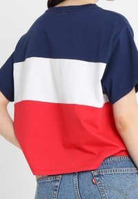 Kratký bavlněný tričko s námořnickými, bílými a červenými vodorovnými pruhy. Neformální design s krátkými rukávy a kulatým výstřihem.