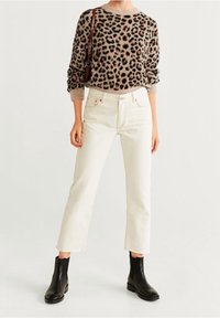 Jersey de punto esponjoso con estampado de leopardo en beige y marrón, combinado con jeans rectos blancos; la modelo lleva botas negras hasta el tobillo.