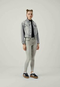 Svijetlosivi traper jakna s dva prednja džepa, crni uski top, svijetlosive uske traperice i crne tenisice s bijelim prugama i smeškim đonom.