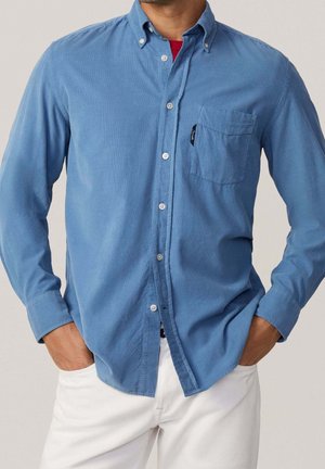 Lichtblauwe button-up shirt van stof met een gladde textuur. Heeft een borstzak en een klassieke kraag. Draagt met witte broek.