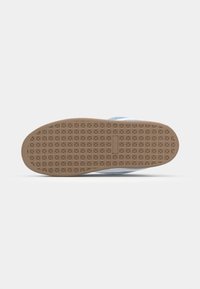 Sola de sapatilha em borracha castanha com um padrão de grip texturizado, apresentando bordas reforçadas e uma leve curvatura na ponta para flexibilidade.