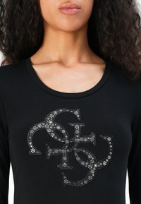 Svart langermet skjorte med et stort, utsmykket logo med sølv detaljer og blomsterdesign på forsiden, rund hals.