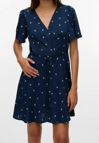 Robe bleu marine avec manches courtes bouffantes, décolleté en V, fermeture à boutons sur le devant et motif à pois vert citron. Comprend une ceinture à la taille pour un ajustement modulable.