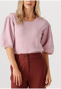Lys rosa strikket sweater med korte, puffede ærmer og rund halsudskæring, parret med højtaljede burgunderbukser med knapdetalje.