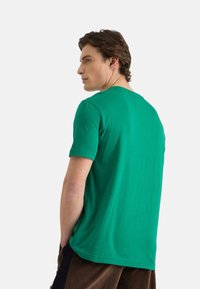 Camiseta verde de manga corta hecha de algodón, con cuello redondo y corte relajado, con textura suave y diseño simple.