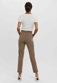 Bruine, taps toelopende broek met een elastische tailleband en achterzakken; gecombineerd met een nauwsluitend wit rib gebreid T-shirt met korte mouwen.