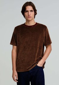 Brunstribet kortærmet T-shirt i blødt tekstureret stof, med en bordeaux rund hals og afslappet pasform. Båret med mørkeblå bukser.