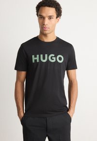 Fekete, pamut póló kerek nyakkal. Az elején nagy, menta zöld "HUGO" felirat található. Egyszerű, rövid ujjú kialakítás.