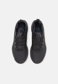 Chaussures de sport noires avec une tige en maille texturée, des lacets ton sur ton et un intérieur rembourré. Comprend un logo réfléchissant sur la languette.