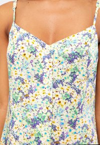 Florales ärmelloses Kleid aus leichtem Stoff mit lila, grünem und gelbem Muster, V-Ausschnitt und weißen Knöpfen vorne.