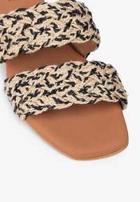 Sandal flat tan que presenta dos anchas bandas trenzadas de fibra natural en beige y negro. Plantilla de imitación de cuero suave. Diseño sencillo.