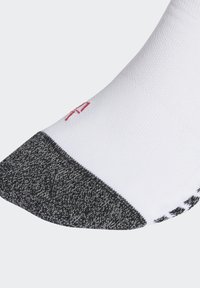 Calcetín blanco con punta y talón grises texturizados. Presenta un detalle del logo rojo cerca de la parte superior. El diseño es de longitud tobillo con un ajuste ceñido.