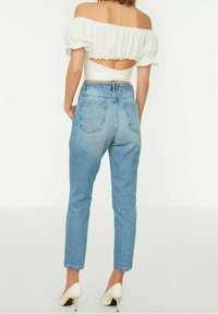 Jeans de mezclilla en azul claro con cintura alta, pierna ajustada y dos bolsillos traseros. Combinados con una blusa blanca sin mangas. Tacones altos blancos.