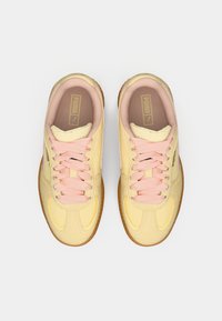 Żółto-kremowe sneakersy z różowymi sznurówkami. Wykonane z miękkiej zamszowej i skórzanej matrycy. Okrągły kształt noska, podeszwa z gumy oraz widoczna marka Puma.