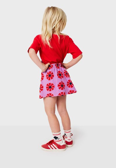 Rød kortærmet T-shirt, lavendel nederdel med rødt blomstermønster, elastisk talje, kombineret med røde sneakers og hvide flæse-sokker.