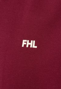 Bordowa tkanina o tkanej fakturze z białym haftowanym logo "FHL" na środku. Prosty design, skupiony na brandingu.