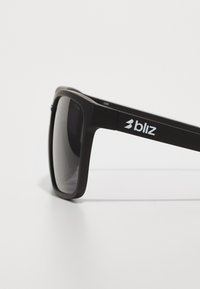 Schwarze Sonnenbrille mit mattem Finish, dicken rechteckigen Rahmen, dunklen Gläsern und weißem "bliz"-Logo an der Seite. Keine zusätzlichen Akzente.