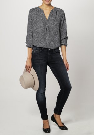 Pitkähihainen, V-niskainen paita, jossa on sinivalkoinen abstrakti kuvio, yhdistettynä tummiin skinny-farkkuihin ja mustiin ballerinatossuihin. Vaalea harmaa hattu pidetään kädessä.