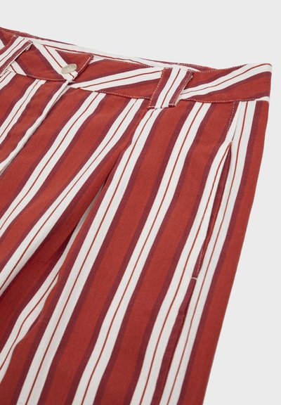 Gros plan d'un pantalon rouge avec des rayures verticales blanches et bordeaux, doté d'une taille boutonnée et de passants pour ceinture.