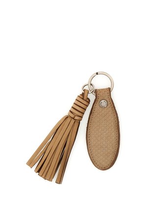 Portachiavi in pelle color cuoio con nappina intrecciata e targhetta ovale di tessuto, attaccati a un anello metallico con cuciture visibili e piccolo bottone metallico.