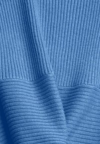 Tissu tricoté côtelé bleu avec des motifs verticaux et horizontaux, montrant des plis et la texture en gros plan.