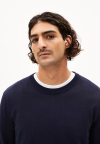 Marineblauwe trui met een geribbelde ronde halslijn en een witte binnenkraag. Glad textuur en aansluitend ontwerp met lange mouwen.