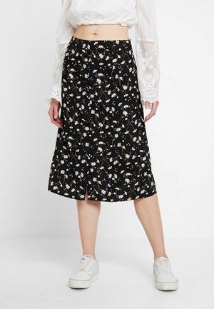 Jupe midi noire avec un motif floral comportant des marguerites blanches, une légère fente et une taille élastique, fabriquée en tissu léger.