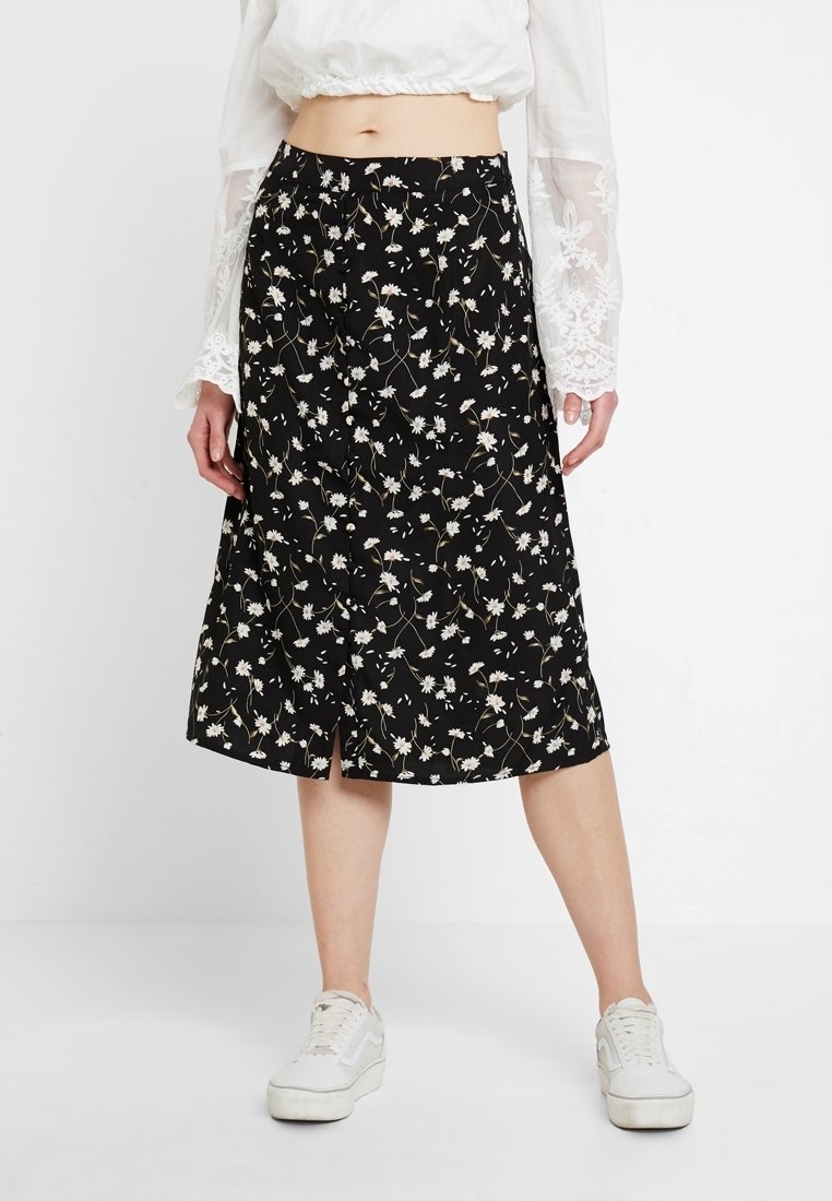 Mustat midi-hame, jossa on kukkakuosi valkoisista päivänkakkaroista, kevyellä kankalla valmistettu, lievä halkio ja joustava vyötärö.