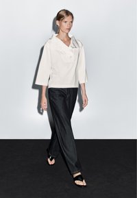 Bílý top s límečkem a kapsou, tříčtvrteční rukávy. Tmavé džíny širokého střihu. Černé sandály na podpatku se páskem přes nohu.