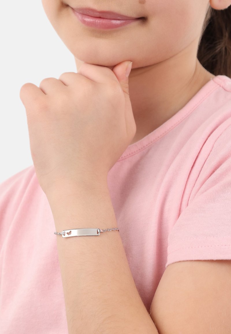 Bracciale d'argento con una barra liscia e piatta caratterizzata da un piccolo cuore ritagliato, attaccato a una delicata catena, indossato sul polso di un bambino.