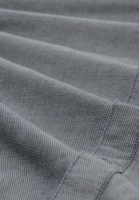 Textilmaterial in Dunkelblau mit gewebter Struktur, das diagonale Falten und feine Muster aufweist und Nähte sowie Stiche betont.