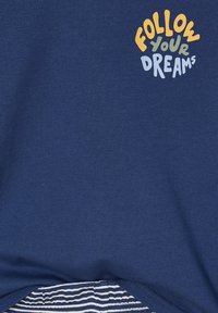 Blauer Stoff mit mehrfarbigem Text "FOLLOW YOUR DREAMS", der nahe der Oberseite aufgedruckt ist, und gestreiftem Stoff, der darunter hervorblitzt.