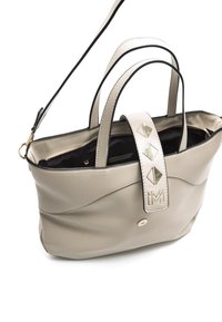 Sac fourre-tout en cuir beige avec des accents brillants et une sangle décorative ornée de clous triangulaires. Il possède des poignées doubles et une poche zippée à l'intérieur.