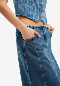 Denimset med en ljusblå, kortärmad knäppväst med traditionella fickor och en matchande högmidjad kjol med fransad nederkant och sidfickor.